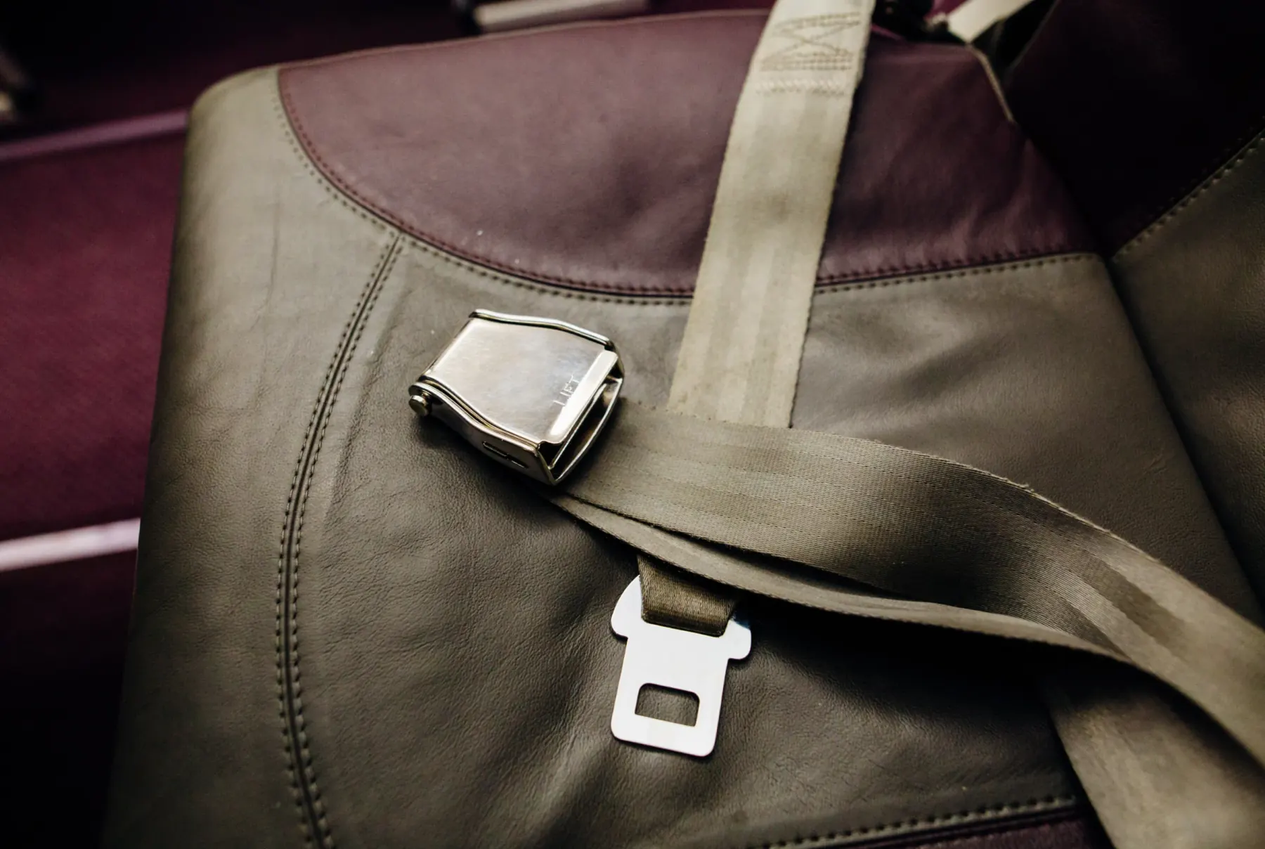 A metal lift-lever lap belt buckle and matching latch plate resting on a leather passenger seat in a specialised transport setting