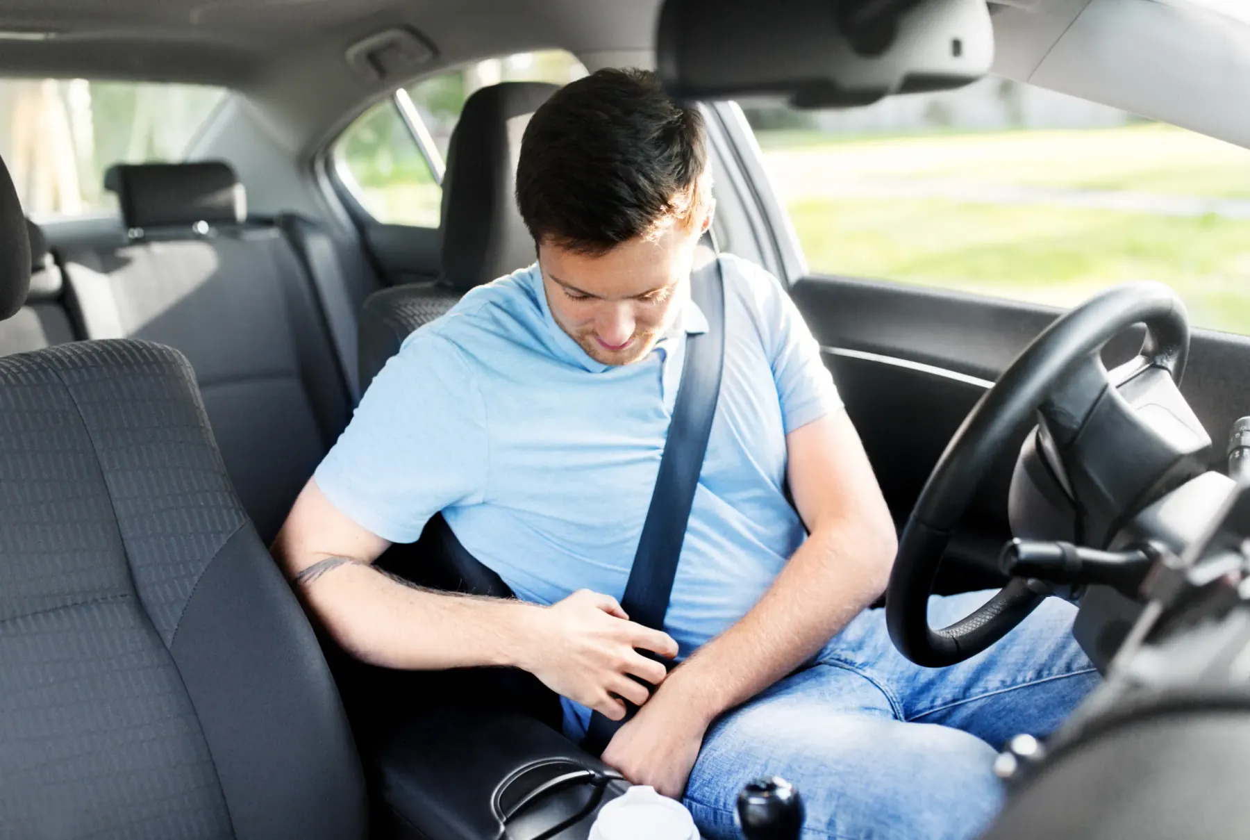 A driver seated in a car adjusting a fastened three-point seat belt across the chest and lap