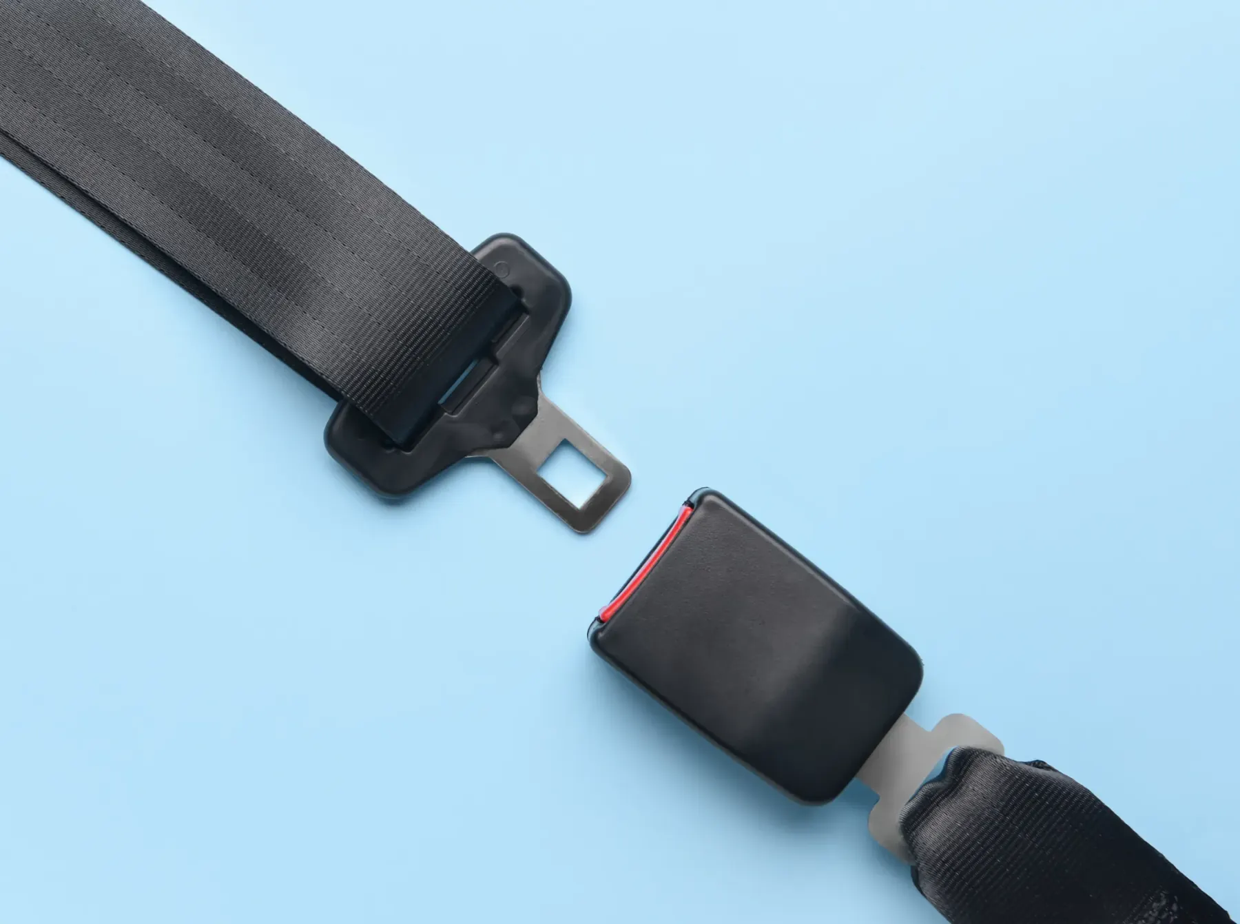 A complete seat belt assembly laid flat on a pale blue background, showing the webbing, the moulded latch plate with its metal tongue, and the separate buckle receptacle