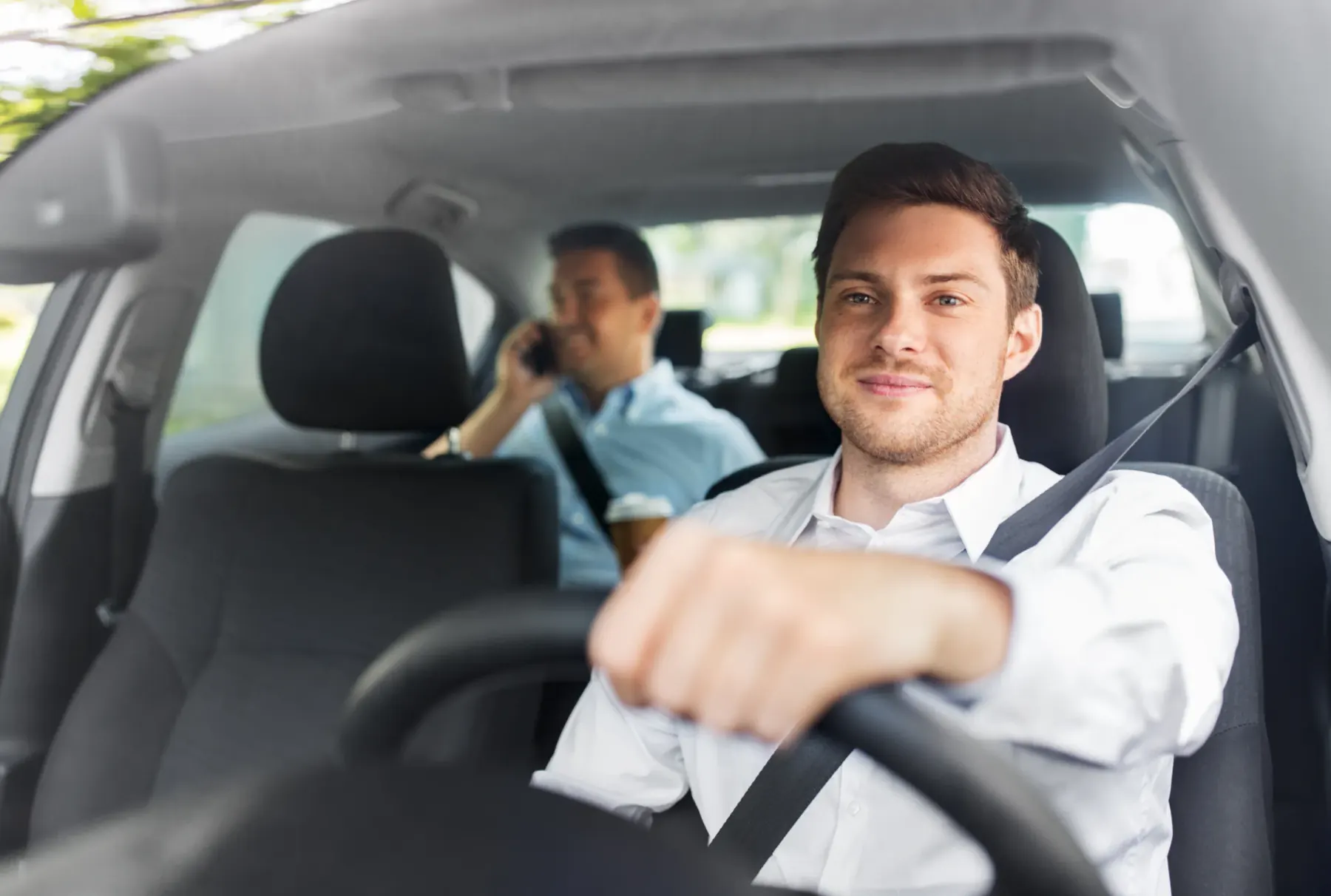 A driver and a rear-seat passenger both wearing fastened three-point seat belts during a journey